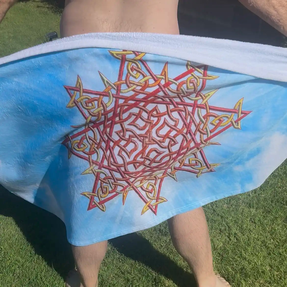 A man shown drying off his behind using a Xigfireon beach towel featuring the Morning Star Fire Celtic knot, Fire Colour On Sky edition.