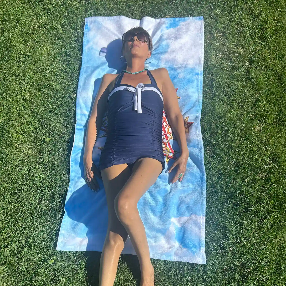 A young lady shown sunbathing on a Xigfireon beach towel featuring the Fire Colour iteration of the Morning Star Fire Celtic knot.