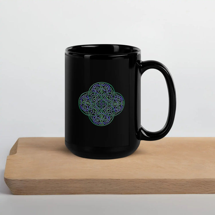 On top of a cutting board, a Xigfireon black ceramic 15oz mug featuring the Living Colour iteration of the Reach Of The Spirit Celtic knot design. This Celtic knot symbolizes Mother Earth.
