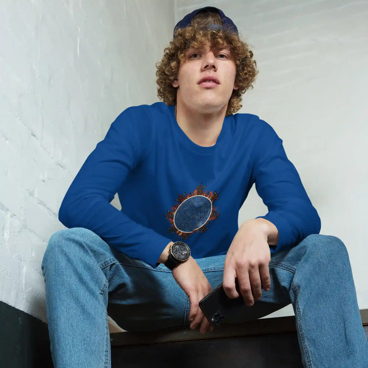 A young man wearing a true royal blue Xigfireon long sleeve graphic tee featuring the Eclipsed iteration of the Morning Star Fire Celtic knot design, inspired by the 2023 Annular Solar Eclipse.