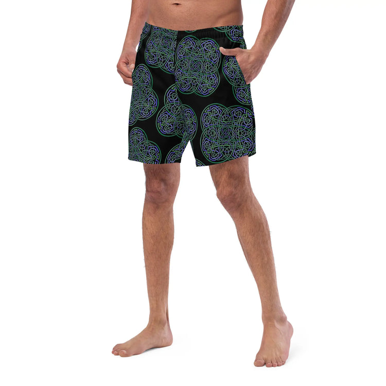 A young man wearing a pair of Xigfireon graphic swim trunks featuring the Living Colour Black patterned series of the Reach Of The Spirit Celtic knot design.