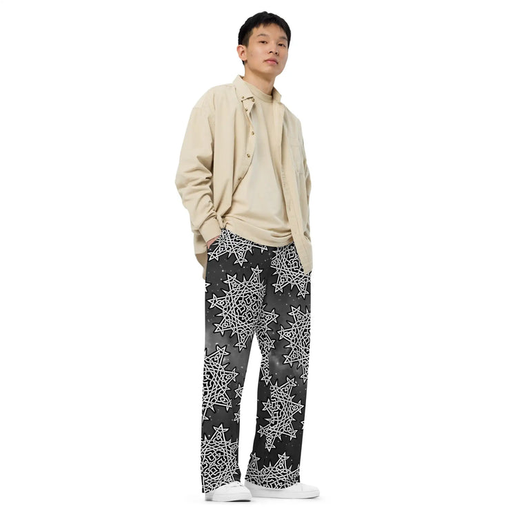 A young man wearing a pair of Xigfireon graphic wide leg pants featuring the Black and White Solid Cosmos patterned series of the Morning Star Fire Celtic knot design.