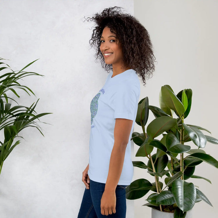 A young woman wearing a baby blue Xigfireon graphic t-shirt featuring the Living Colour iteration of the `Reach Of The Spirit` Celtic knot design along with a message in a Celtic font: "Our Mother, Cherish Her".