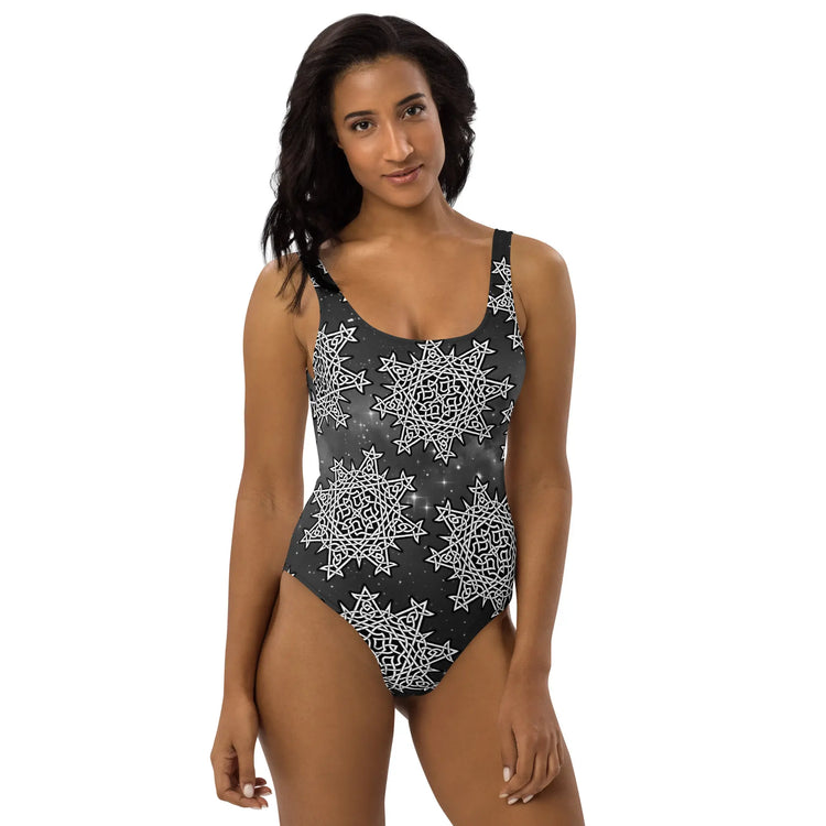 A woman, viewed from the front, wearing a Xigfireon graphic swimsuit featuring the Black & White Solid Cosmos patterned series of the `Morning Star Fire` Celtic knot design.