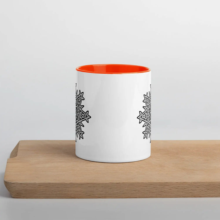 A cutting board displaying a Xigfireon white ceramic 11oz mug featuring the Black & White Solid iteration of the `Morning Star Fire` Celtic knot design, with orange handle and inside. This Celtic knot symbolizes Father Sun.