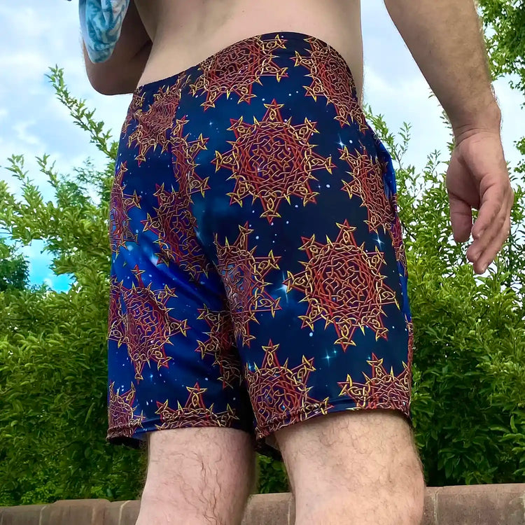 A man, viewed from behind, wearing a pair of Xigfireon graphic swim trunks featuring the Fire Colour Cosmos (small) patterned series of the `Morning Star Fire` Celtic knot design.