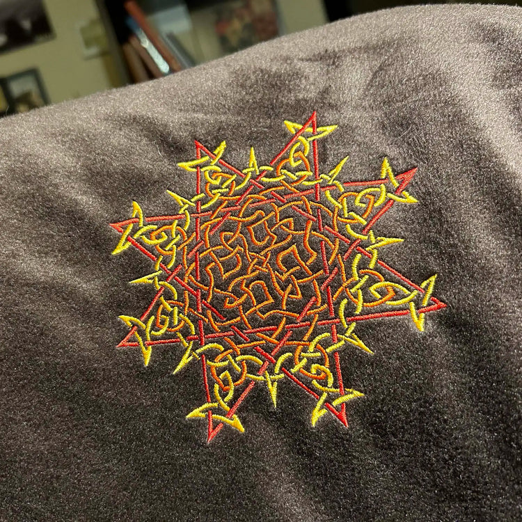 A close-up of a fireside brown Xigfireon sherpa blanket embroidered with the Fire Colour iteration of the `Morning Star Fire` Celtic knot design. The `Morning Star Fire` Celtic knot represents Father Sun.