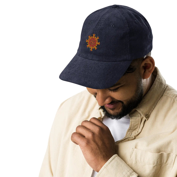 A young man wearing a navy blue Xigfireon vintage corduroy cap embroidered with the Fire Colour iteration of the `Morning Star Fire` Celtic knot design.