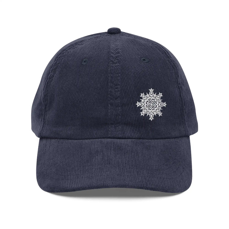The front side of a navy blue Xigfireon vintage corduroy cap embroidered with the White iteration of the `Morning Star Fire` Celtic knot design offset to the left.