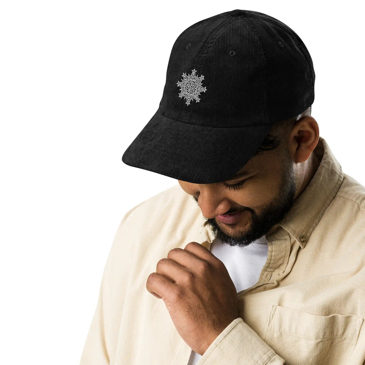 A young man wearing a black Xigfireon vintage corduroy cap embroidered with the White iteration of the `Morning Star Fire` Celtic knot design.