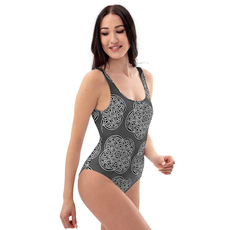 A woman, viewed from the front, wearing a Xigfireon graphic swimsuit featuring the Black & White Solid Forest patterned series of the `Reach Of The Spirit` Celtic knot design.