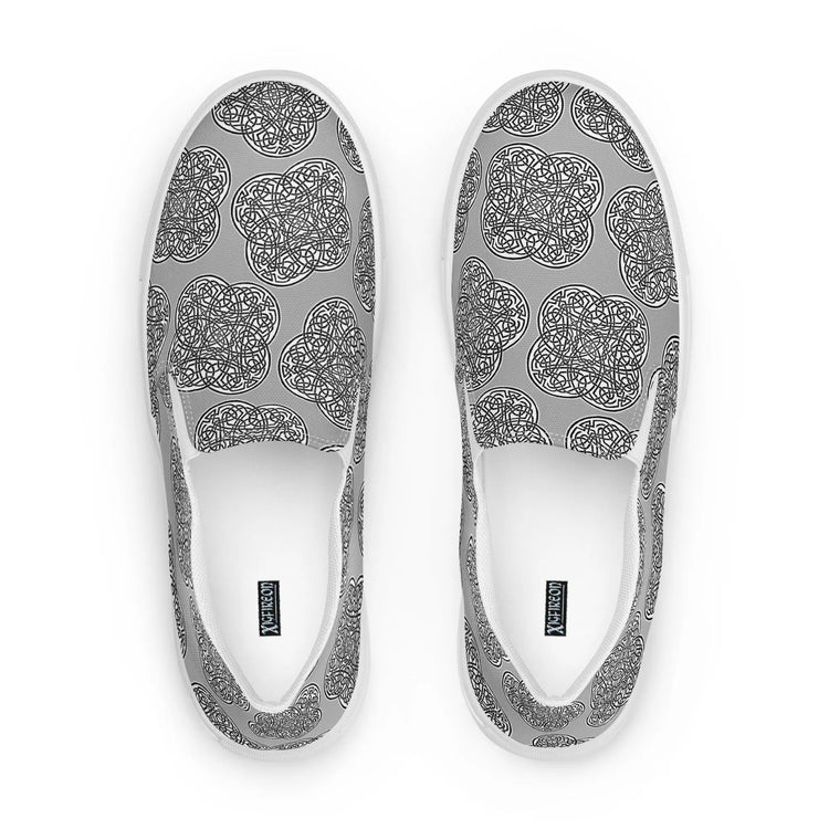 A view from above of a pair of Xigfireon canvas slip-ons featuring the Inverted Black & White Solid iteration of the `Reach of The Spirit` Celtic knot pattern. The Xigfireon logo is visible inside each shoe.