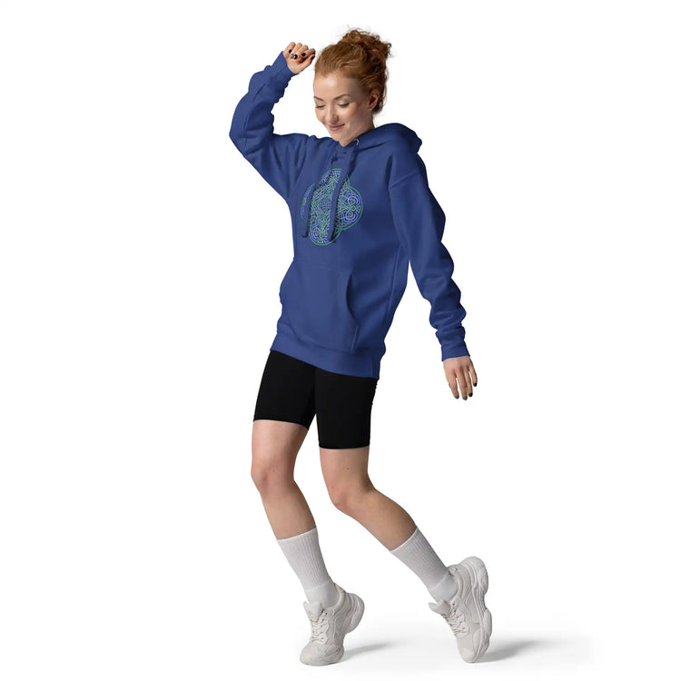 A young woman wearing a team royal blue Xigfireon graphic hoodie featuring the Living Colour Flat iteration of the `Reach Of The Spirit` Celtic knot design. The `Reach Of The Spirit` Celtic knot symbolizes the Earth.