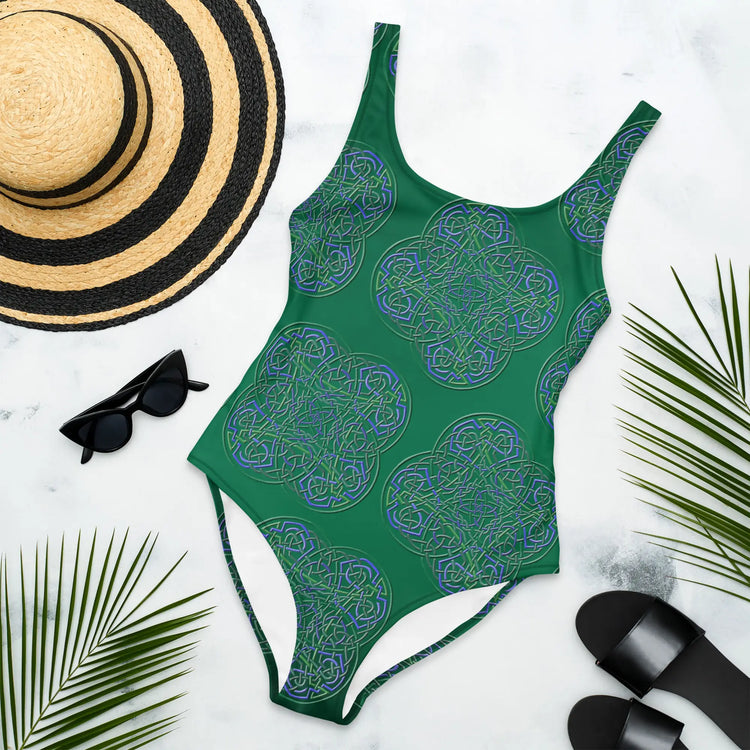 A sunhat, sun glasses, and beach sandals displayed with a Xigfireon graphic swimsuit featuring the Living Colour Forest patterned series of the `Reach Of The Spirit` Celtic knot design.