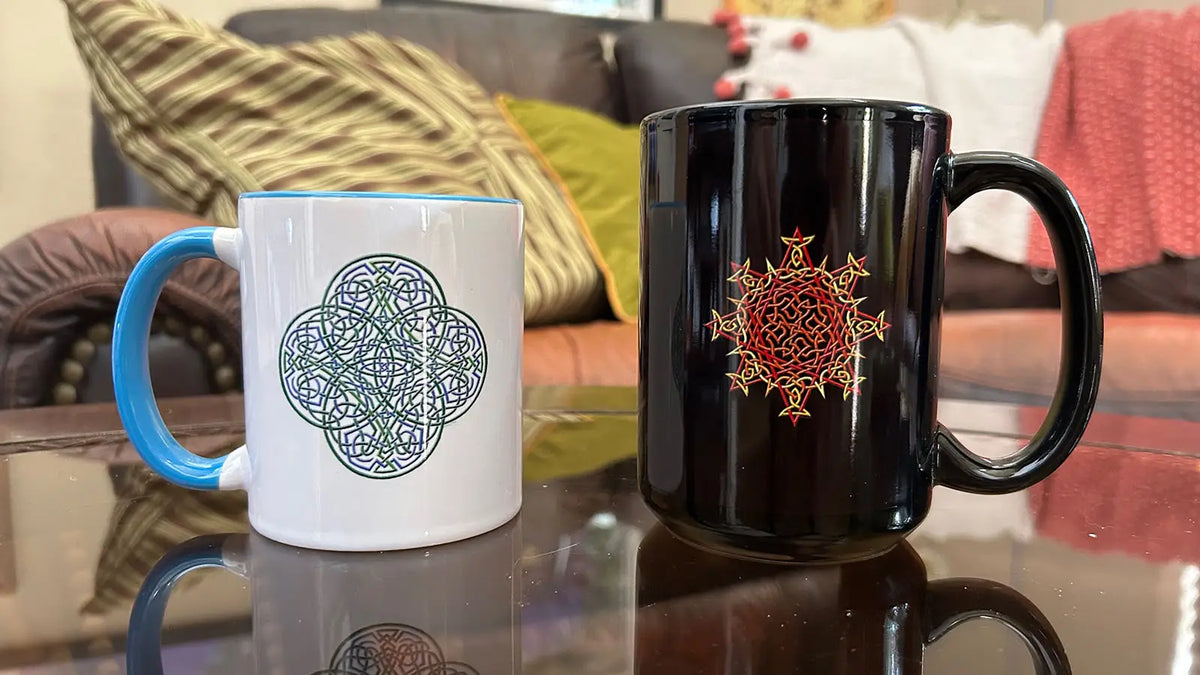Reach of The Spirit (white with blue inside) and Morning Star Fire (black) ceramic mugs on a coffee table.