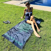 A young lady shown sunbathing near a pool on a Xigfireon beach towel featuring the Celestial iteration of the `Morning Star Fire` Celtic knot.