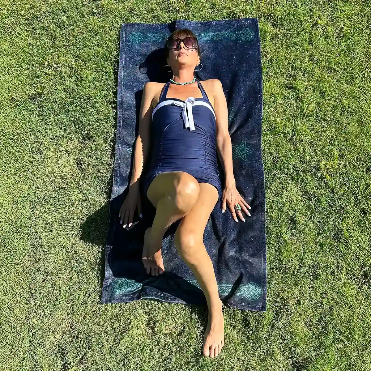 A young lady shown sunbathing on a Xigfireon beach towel featuring the Celestial iteration of the Morning Star Fire Celtic knot.