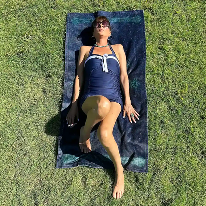 A young lady shown sunbathing on a Xigfireon beach towel featuring the Celestial iteration of the Morning Star Fire Celtic knot.