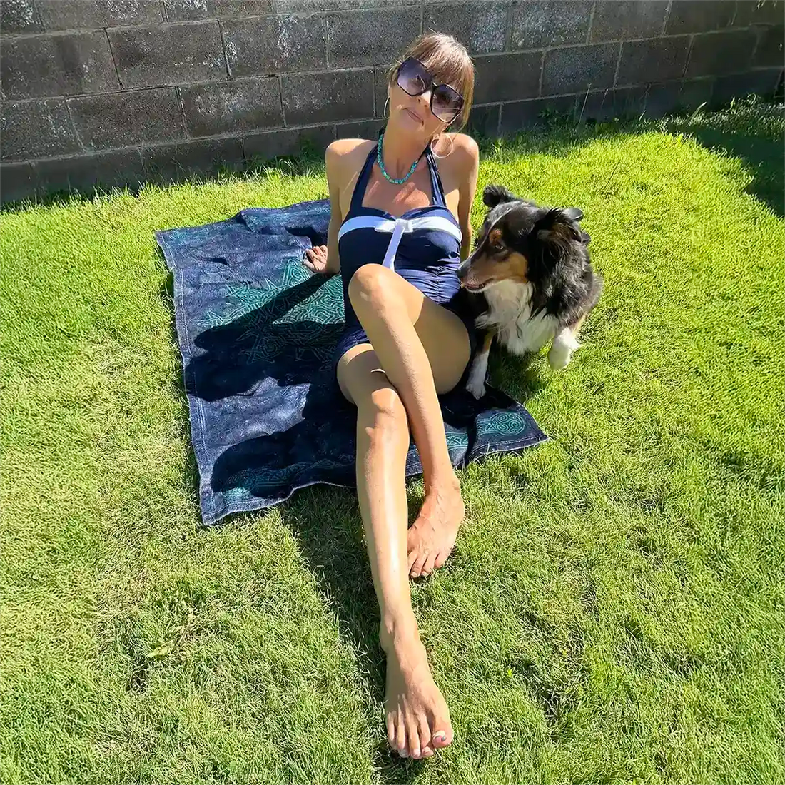 A young lady with her dog shown sunbathing on a Xigfireon beach towel featuring the Celestial iteration of the Morning Star Fire Celtic knot.