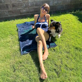A young lady with her dog shown sunbathing on a Xigfireon beach towel featuring the Celestial iteration of the `Morning Star Fire` Celtic knot.