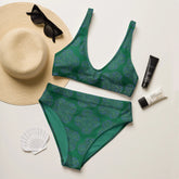 A view of a sunhat, sun glasses, and sunscreen displayed around a Xigfireon graphic bikini featuring the Living Colour Forest patterned series of the Reach Of The Spirit Celtic knot design.