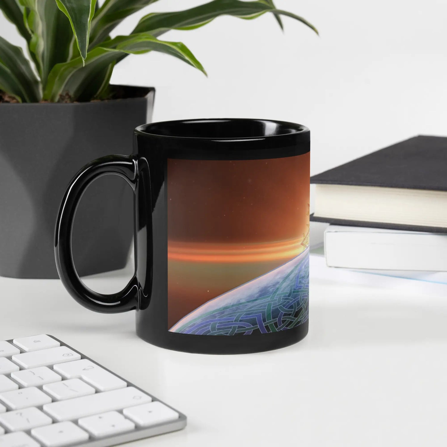 An office desk displaying an 11oz Xigfireon black glossy graphic mug featuring the Derivation II Celtic knots merger design.