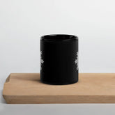 A Xigfireon black glossy 11oz mug, featuring the Black & White Solid iteration of the Morning Star Fire Celtic knot design, sitting on a cutting board. This Celtic knot symbolizes Father Sun.