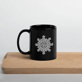 A Xigfireon black glossy 11oz mug featuring the Black & White Solid iteration of the Morning Star Fire Celtic knot design sitting on a cutting board. This Celtic knot symbolizes Father Sun.