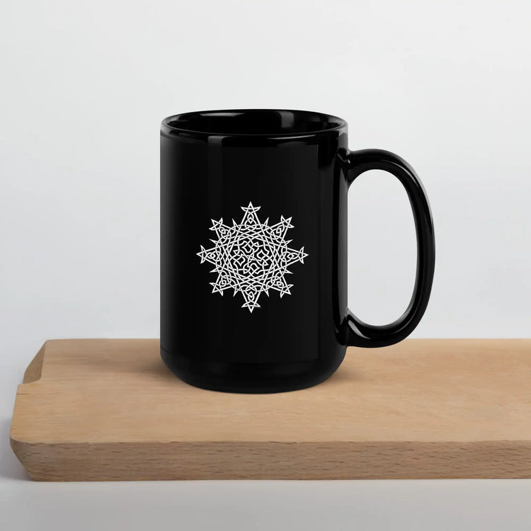 A cutting board beneath a Xigfireon black glossy 15oz mug featuring the Black & White Solid iteration of the Morning Star Fire Celtic knot design. This Celtic knot symbolizes Father Sun.
