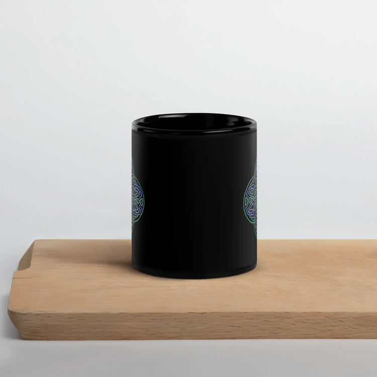 A cutting board displaying a Xigfireon black ceramic 11oz mug featuring the Living Colour iteration of the Reach Of The Spirit Celtic knot design. This Celtic knot symbolizes Mother Earth.