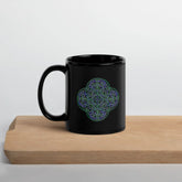 A cutting board displaying a Xigfireon black ceramic 11oz mug featuring the Living Colour iteration of the Reach Of The Spirit Celtic knot design. This Celtic knot symbolizes Mother Earth.