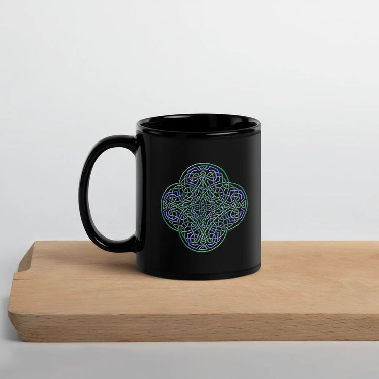 A cutting board displaying a Xigfireon black ceramic 11oz mug featuring the Living Colour iteration of the Reach Of The Spirit Celtic knot design. This Celtic knot symbolizes Mother Earth.