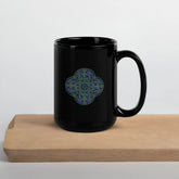 On top of a cutting board, a Xigfireon black ceramic 15oz mug featuring the Living Colour iteration of the Reach Of The Spirit Celtic knot design. This Celtic knot symbolizes Mother Earth.