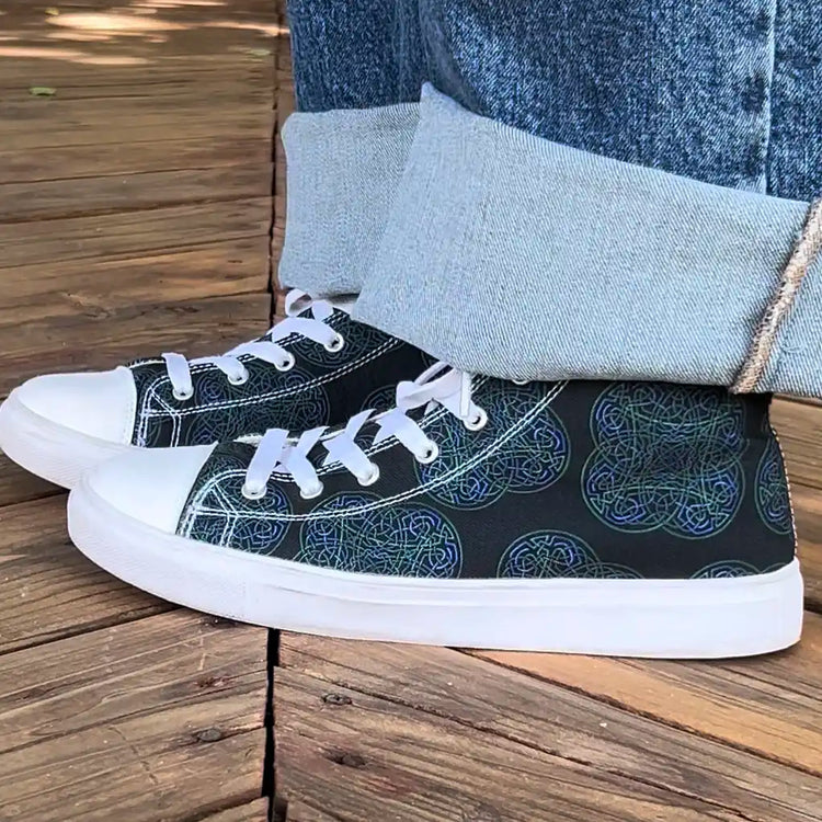 Canvas high top shoes worn with jeans, viewed from the side, featuring the Living Colour iteration of the Reach Of The Spirit Celtic knot pattern.
