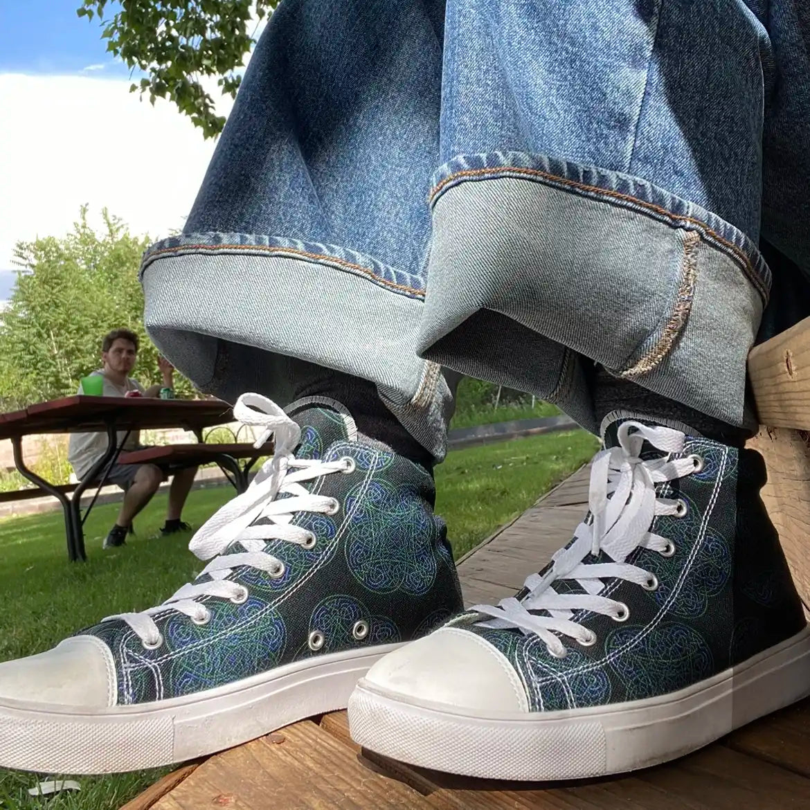 Canvas high top shoes worn with jeans, viewed from front left, featuring the Living Colour iteration of the Reach Of The Spirit Celtic knot pattern.