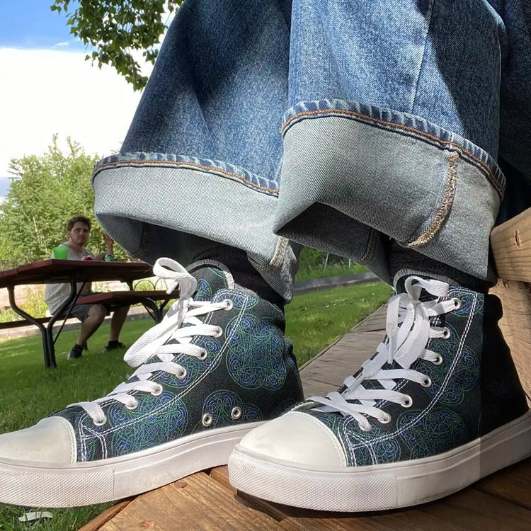 Canvas high top shoes worn with jeans, viewed from front left, featuring the Living Colour iteration of the Reach Of The Spirit Celtic knot pattern.