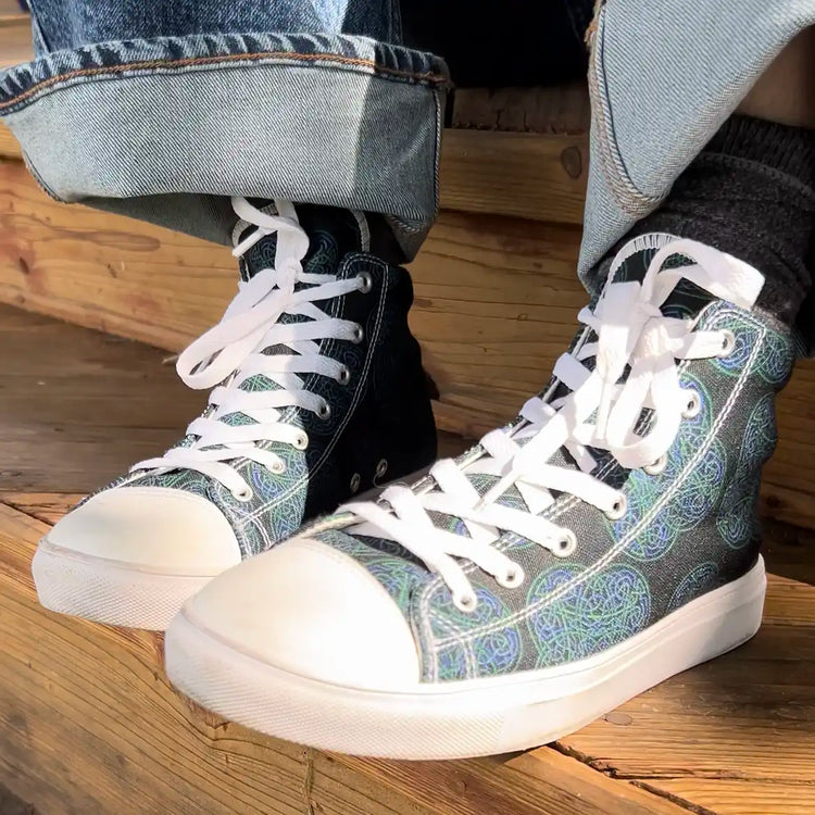 Canvas high top shoes worn with jeans, viewed from front left, featuring the Living Colour iteration of the Reach Of The Spirit Celtic knot pattern.