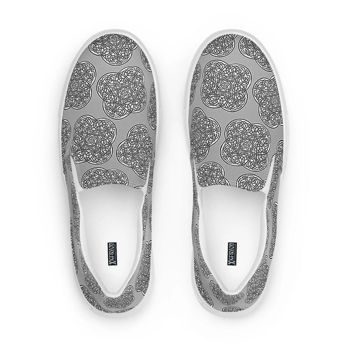 A view from above of a pair of Xigfireon canvas slip-ons featuring the Inverted Black &amp; White Solid iteration of the Reach of The Spirit Celtic knot pattern. The Xigfireon logo is visible inside each shoe.