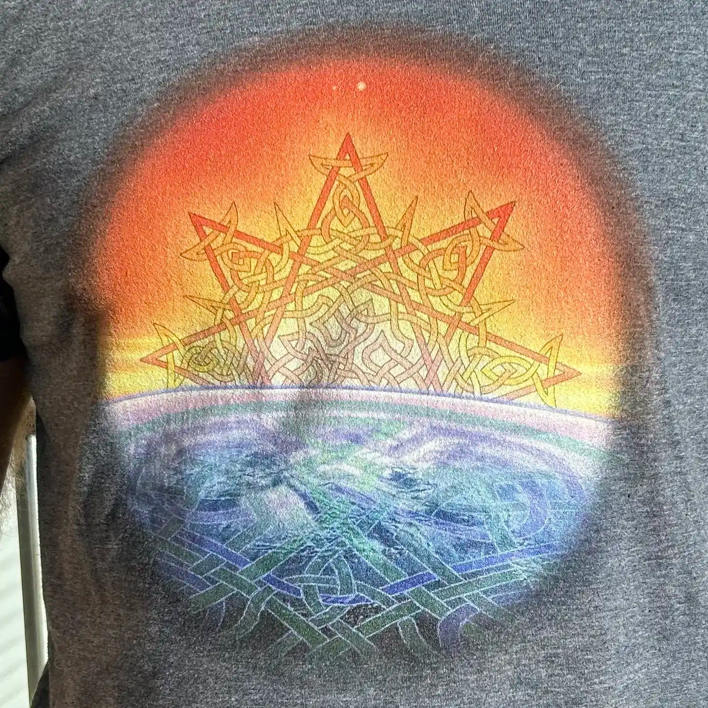 A close up of a gentleman wearing a dark heather Xigfireon graphic t-shirt featuring the Derivation II Celtic knots merger design.