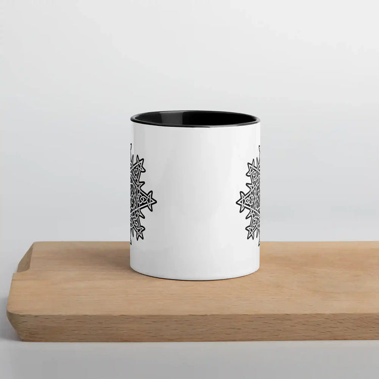 A cutting board displaying a Xigfireon white ceramic 11oz mug featuring the Black & White Solid iteration of the Morning Star Fire Celtic knot design, with black handle and inside. This Celtic knot symbolizes Father Sun.