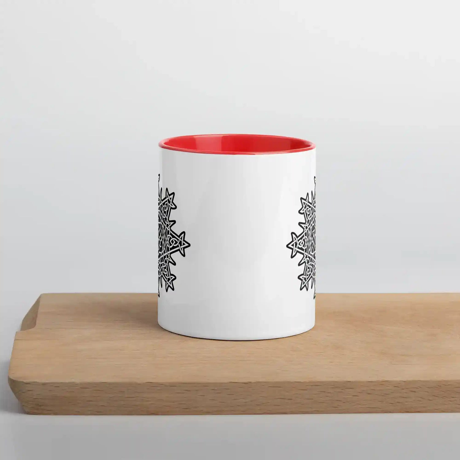 A cutting board dislaying a Xigfireon white ceramic 11oz mug featuring the Black & White Solid iteration of the Morning Star Fire Celtic knot design, with red handle and inside. This Celtic knot symbolizes Father Sun.
