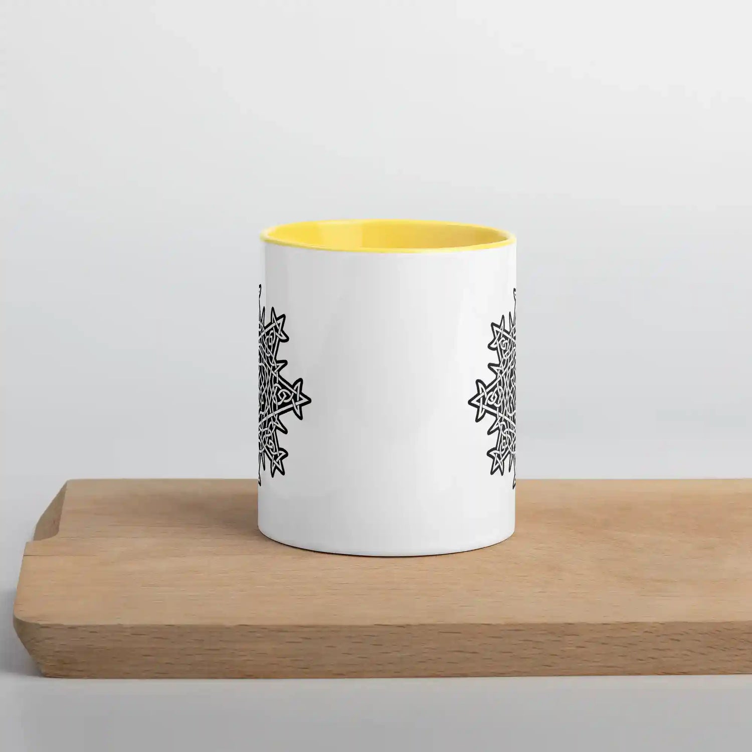 The front side of a Xigfireon white ceramic 11oz mug featuring the Black & White Solid iteration of the Morning Star Fire Celtic knot design, with yellow handle and inside. This Celtic knot symbolizes Father Sun.