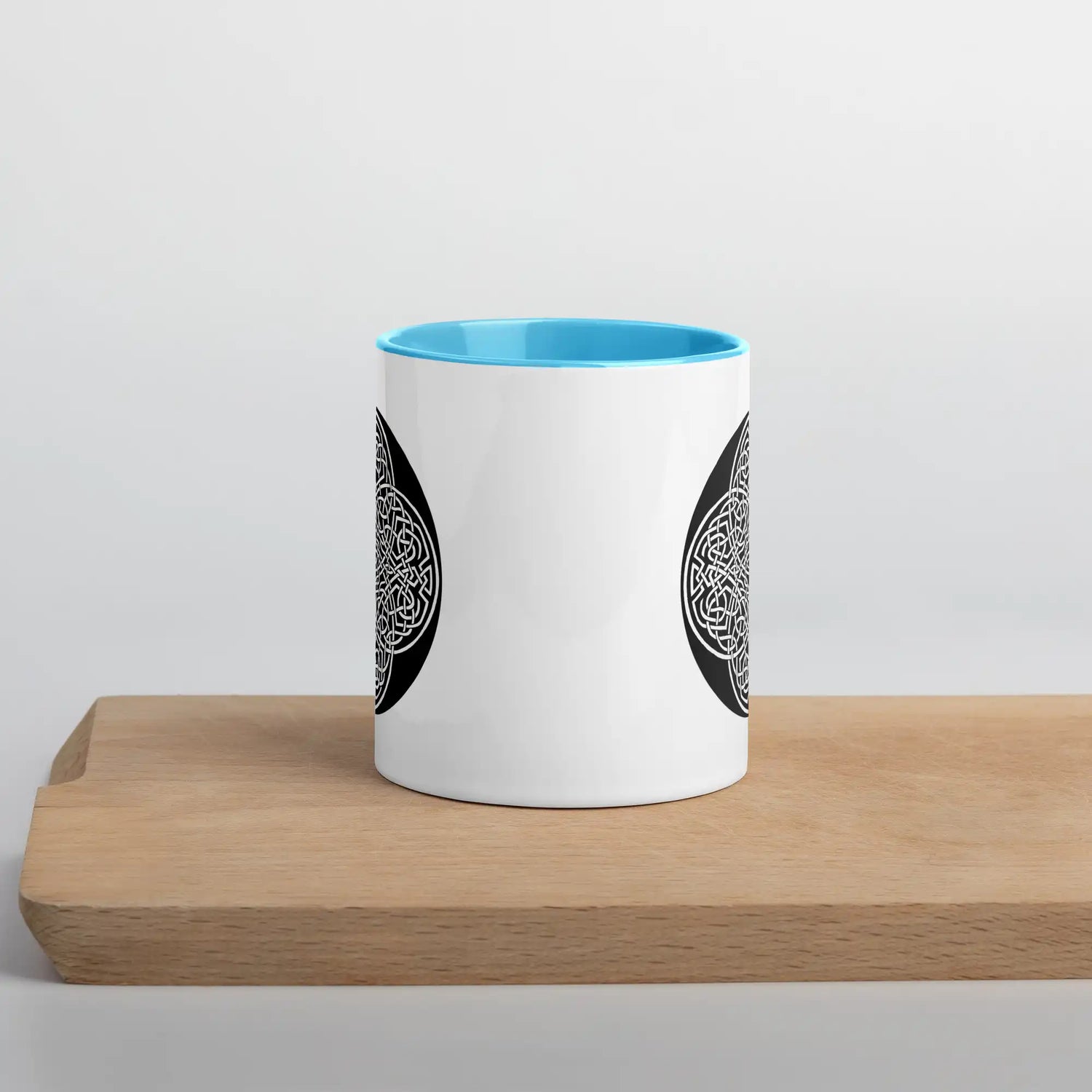 A Xigfireon white ceramic 11oz mug featuring the Black & White Circle iteration of the Reach Of The Spirit Celtic knot design, with blue handle and inside. This Celtic knot symbolizes Mother Earth.