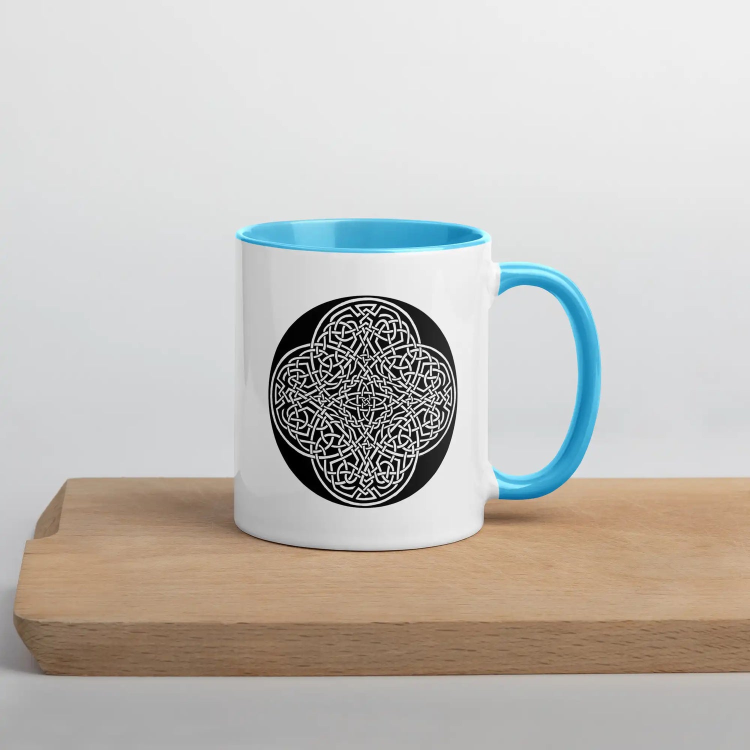 A Xigfireon white ceramic 11oz mug featuring the Black & White Circle iteration of the Reach Of The Spirit Celtic knot design, with blue handle and inside. This Celtic knot symbolizes Mother Earth.