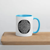 A Xigfireon white ceramic 11oz mug featuring the Black & White Circle iteration of the Reach Of The Spirit Celtic knot design, with blue handle and inside. This Celtic knot symbolizes Mother Earth.