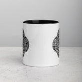 A tabletop displaying a Xigfireon white ceramic 11oz mug featuring the Black & White Solid iteration of the Reach Of The Spirit Celtic knot design, with black handle and inside. This Celtic knot symbolizes Mother Earth.