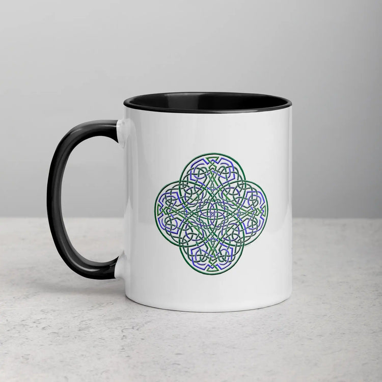 A tabletop displaying a Xigfireon white ceramic 11oz mug featuring the Living Colour iteration of the Reach Of The Spirit Celtic knot design, with black handle and inside. This Celtic knot symbolizes Mother Earth.