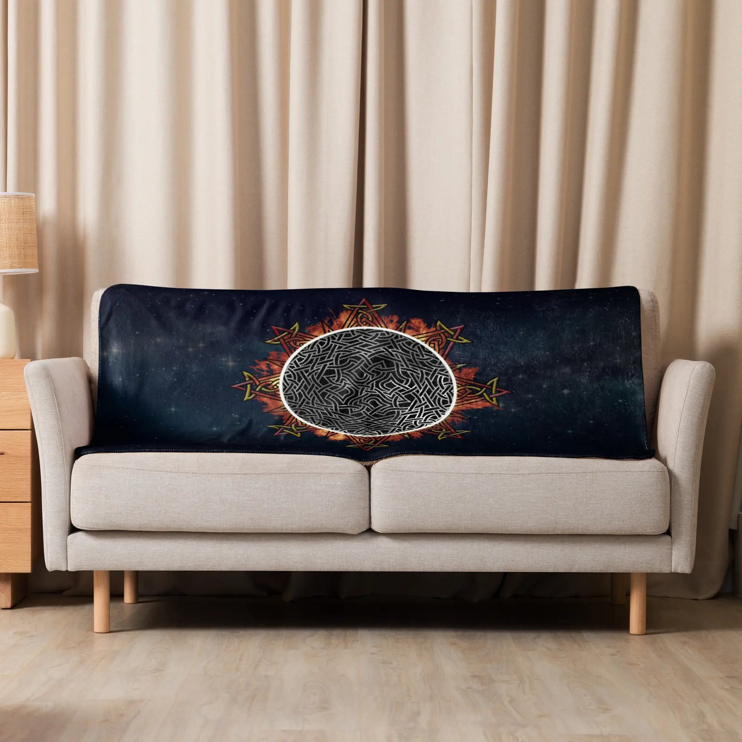 A sofa covered by a 37 inch by 57 inch Xigfireon sublimated sherpa blanket featuring the Eclipsed iteration of the Morning Star Fire Celtic knot design. Inspired by the 2023 Annular Solar Eclipse.