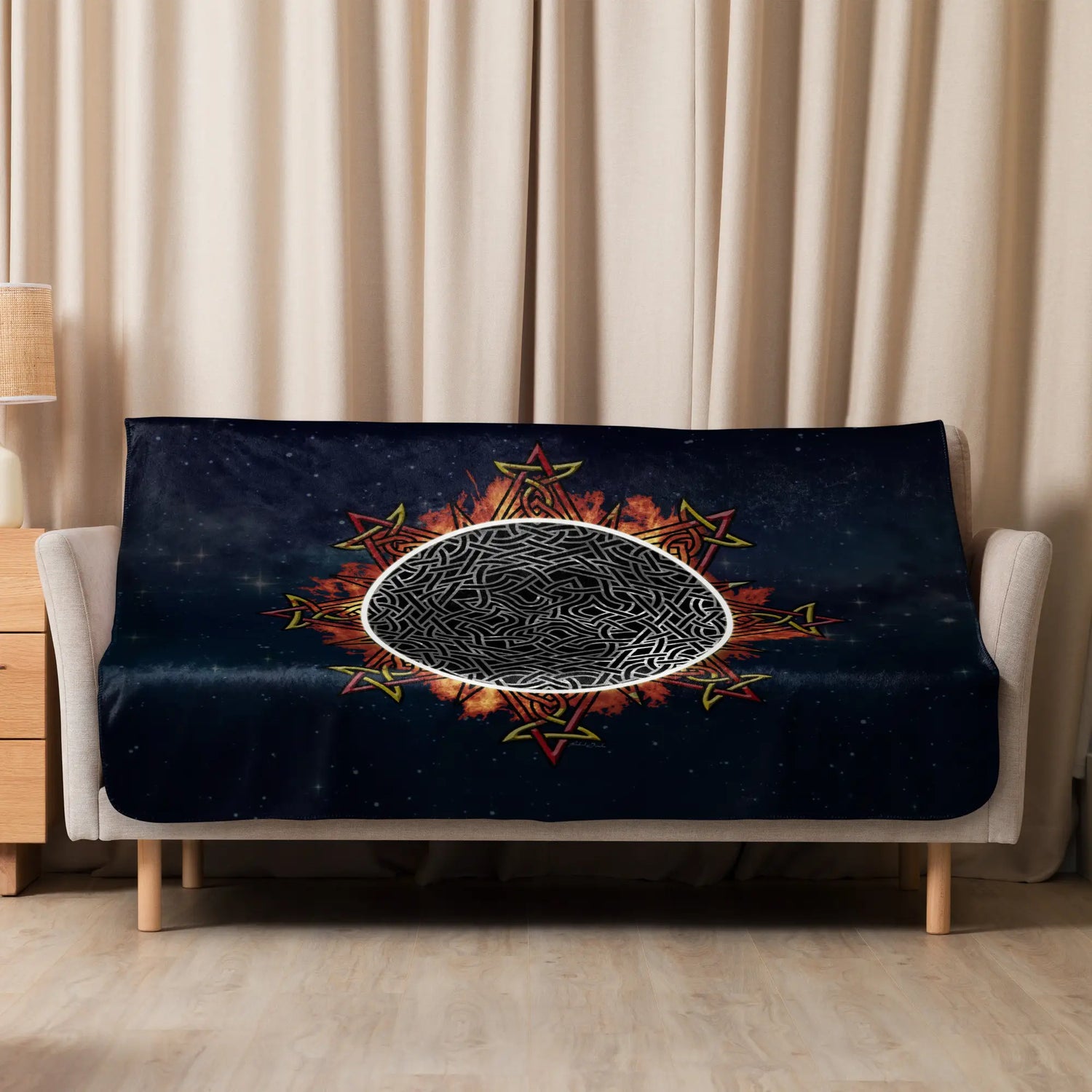 A sofa covered by a 50 inch by 60 inch Xigfireon sublimated sherpa blanket featuring the Eclipsed iteration of the Morning Star Fire Celtic knot design. Inspired by the 2023 Annular Solar Eclipse.