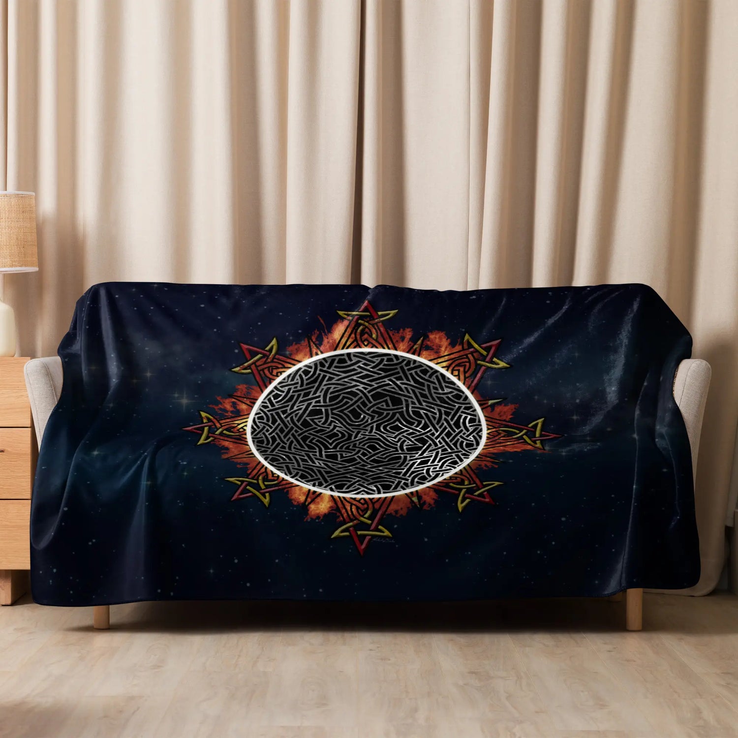 A sofa covered by a 60 inch by 80 inch Xigfireon sublimated sherpa blanket featuring the Eclipsed iteration of the Morning Star Fire Celtic knot design. Inspired by the 2023 Annular Solar Eclipse.